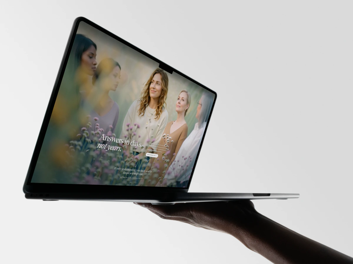 A hand holding an open laptop showing the Nura Health homepage, Answers in days, not years.