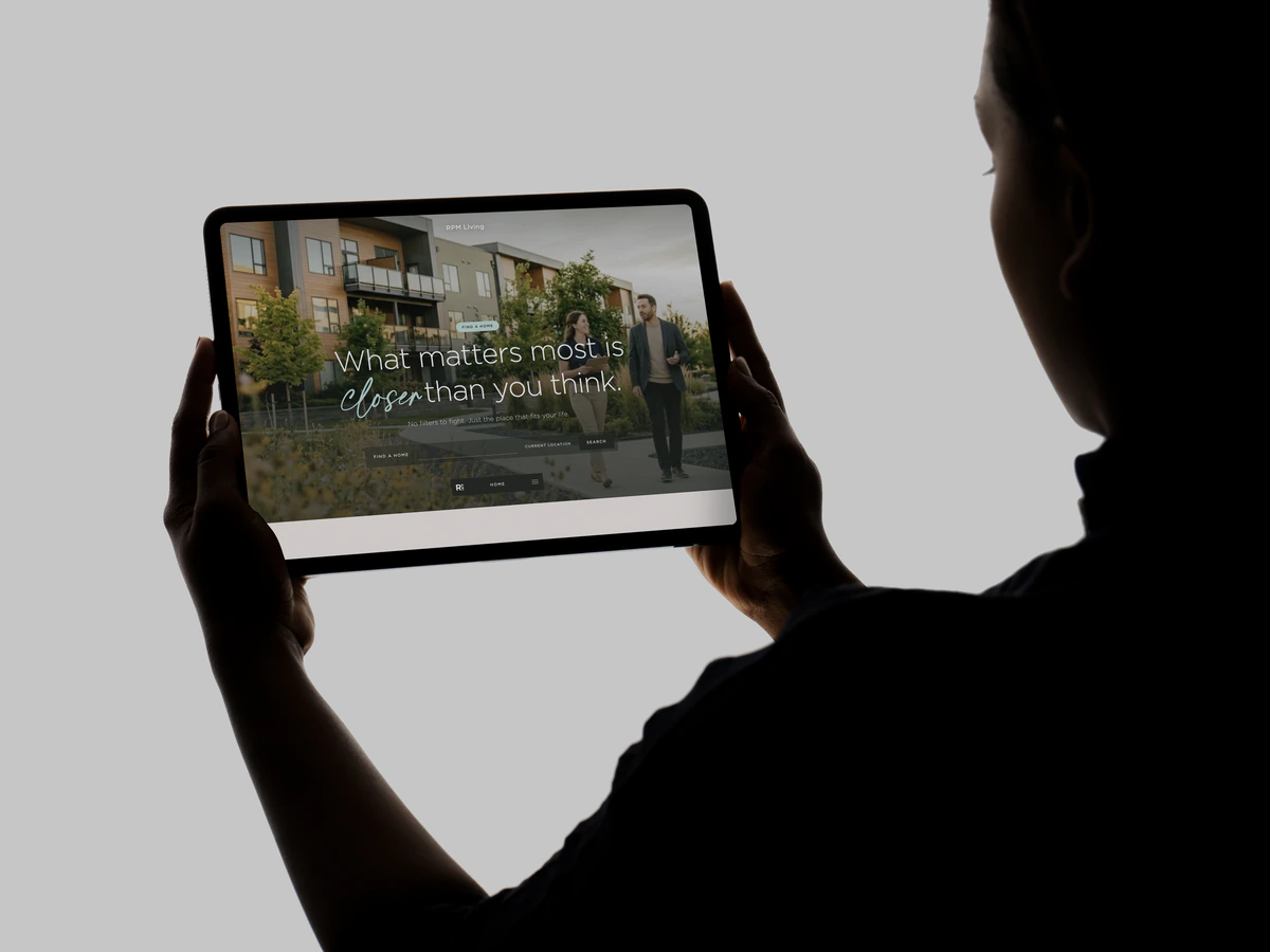 Silhouette holding a tablet showing the RPM Living apartment search homepage
